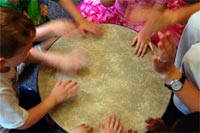 Photo of kids beating on a large drum.