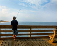 Photo of man fishing off a pier on the coast of North Carolina.