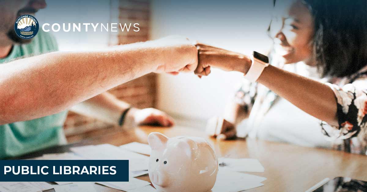 An interracial couple fist bumps while they are working on their finance. A piggy bank is in the foreground. 